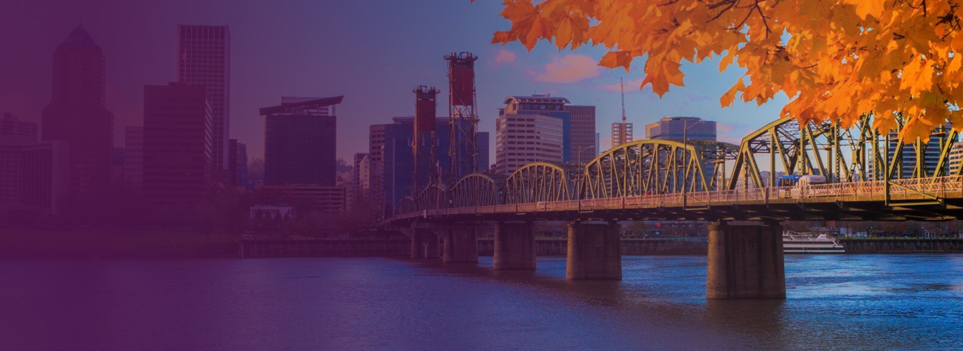 View of a city skyline with a yellow arched bridge over a river and autumn orange leaves in the foreground.