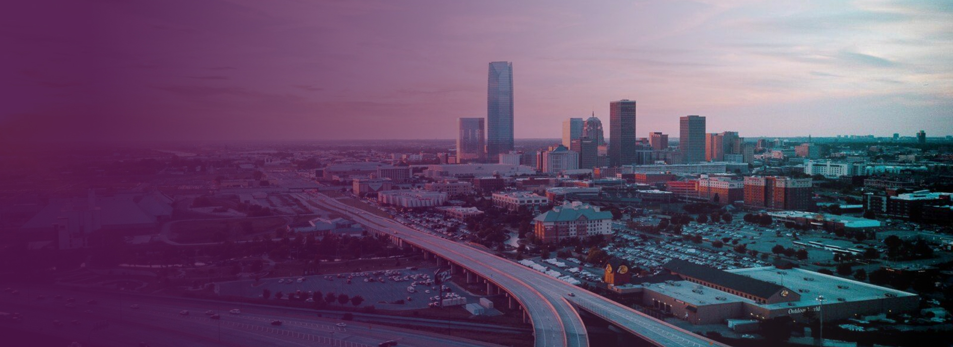 Aerial view of Oklahoma City skyline at dusk with highway curving towards downtown skyscrapers.
