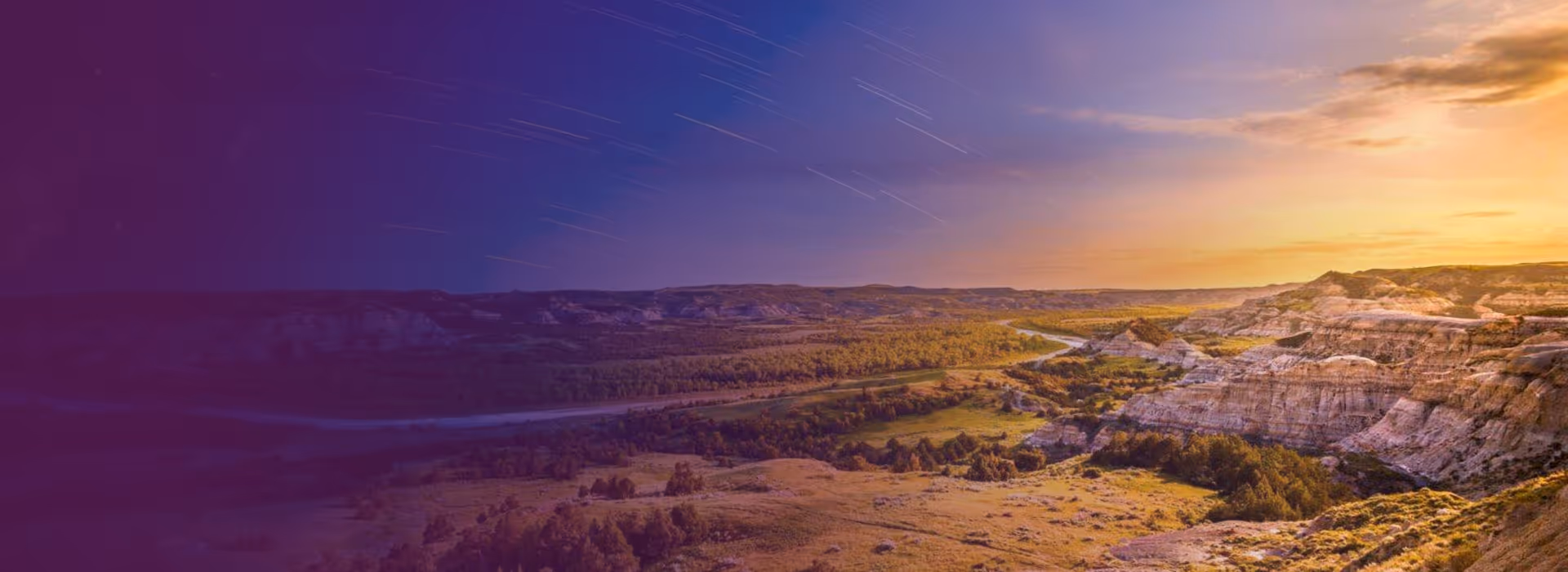 Sunset over North Dakota badlands with a winding river and star trails in the twilight sky.