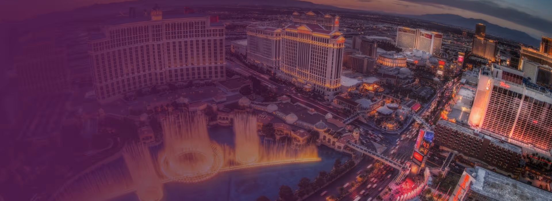 Aerial view of the Las Vegas Strip at dusk with the Bellagio hotel and its illuminated fountain show in the foreground.