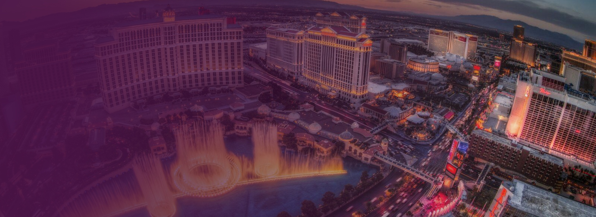Aerial view of the Las Vegas Strip at dusk with the Bellagio hotel and its illuminated fountain show in the foreground.