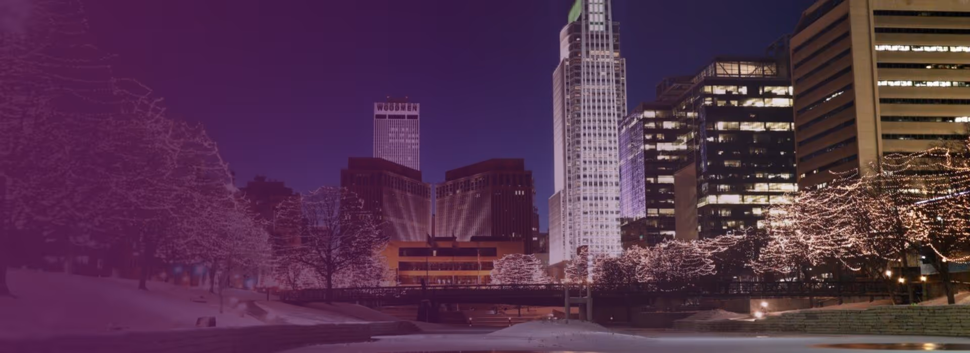 Nighttime cityscape of downtown Omaha, Nebraska with illuminated trees and tall buildings including the Woodmen Tower.