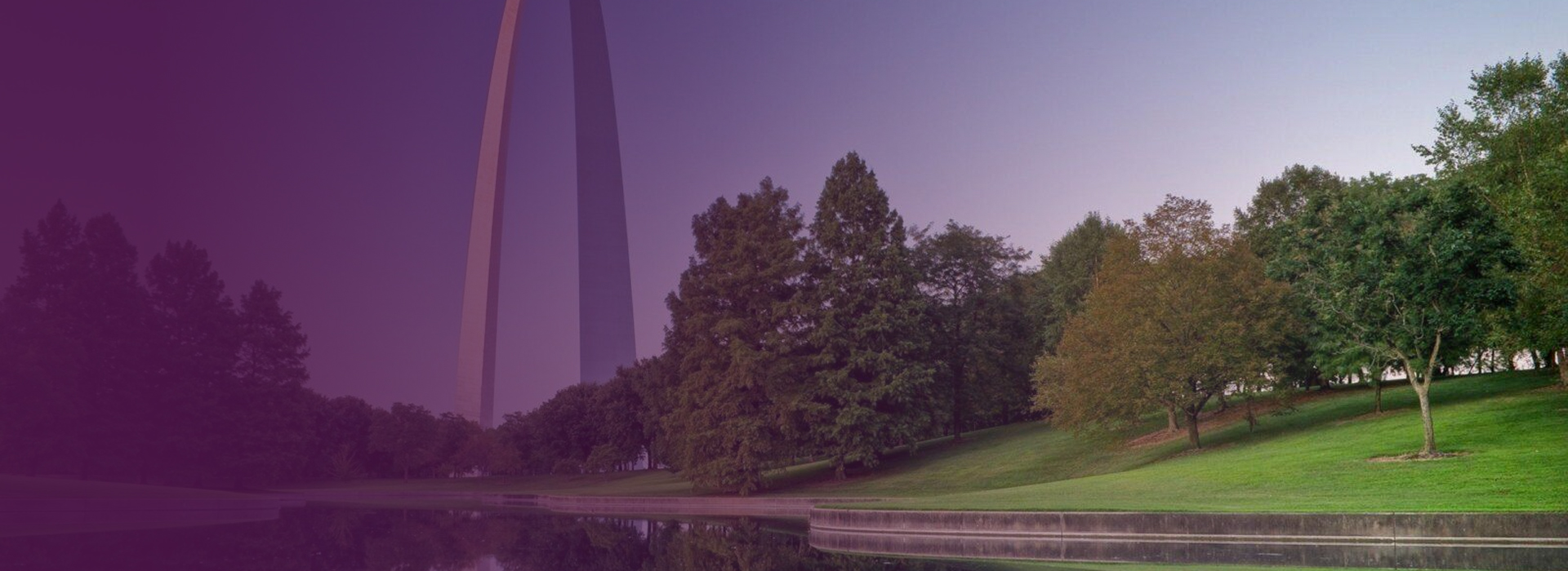 The Gateway Arch towering over a green park with trees reflecting in a calm body of water.