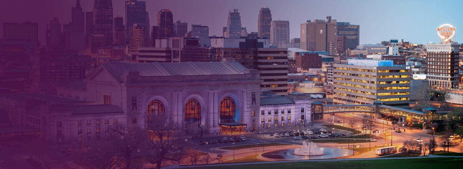 Evening skyline of downtown Kansas City with Union Station and the illuminated Western Auto sign.