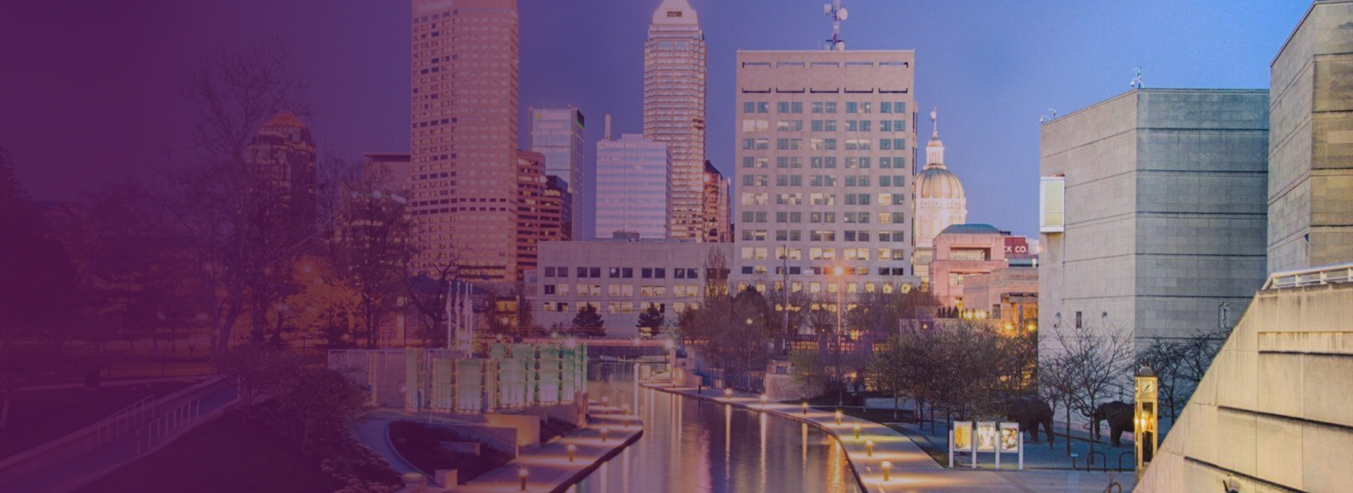 Evening view of downtown Indianapolis skyline with canal and lit pathways.