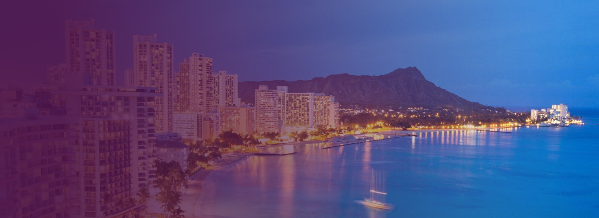 Evening view of Waikiki skyline with lit buildings along the beach and Diamond Head crater in the background in Honolulu, Hawaii.