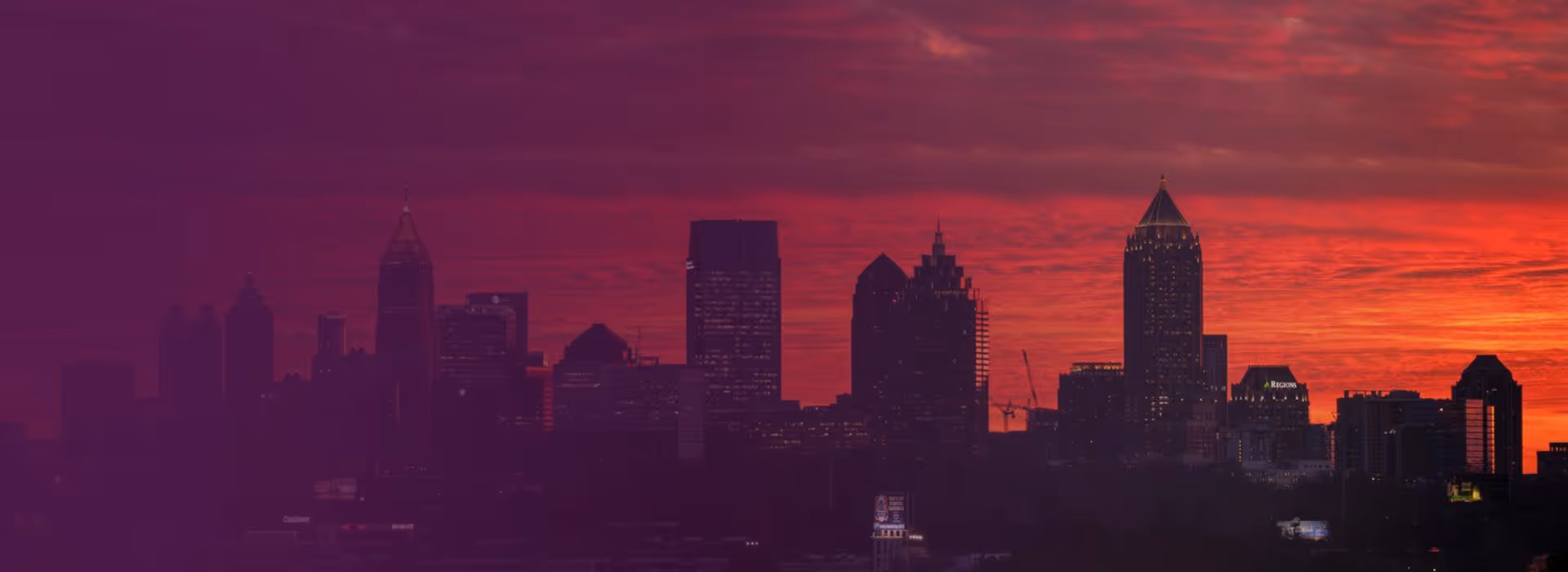 Silhouette of a city skyline at sunset with a vibrant red and orange sky.