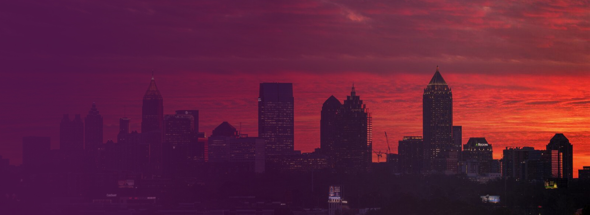 Silhouette of a city skyline at sunset with a vibrant red and orange sky.