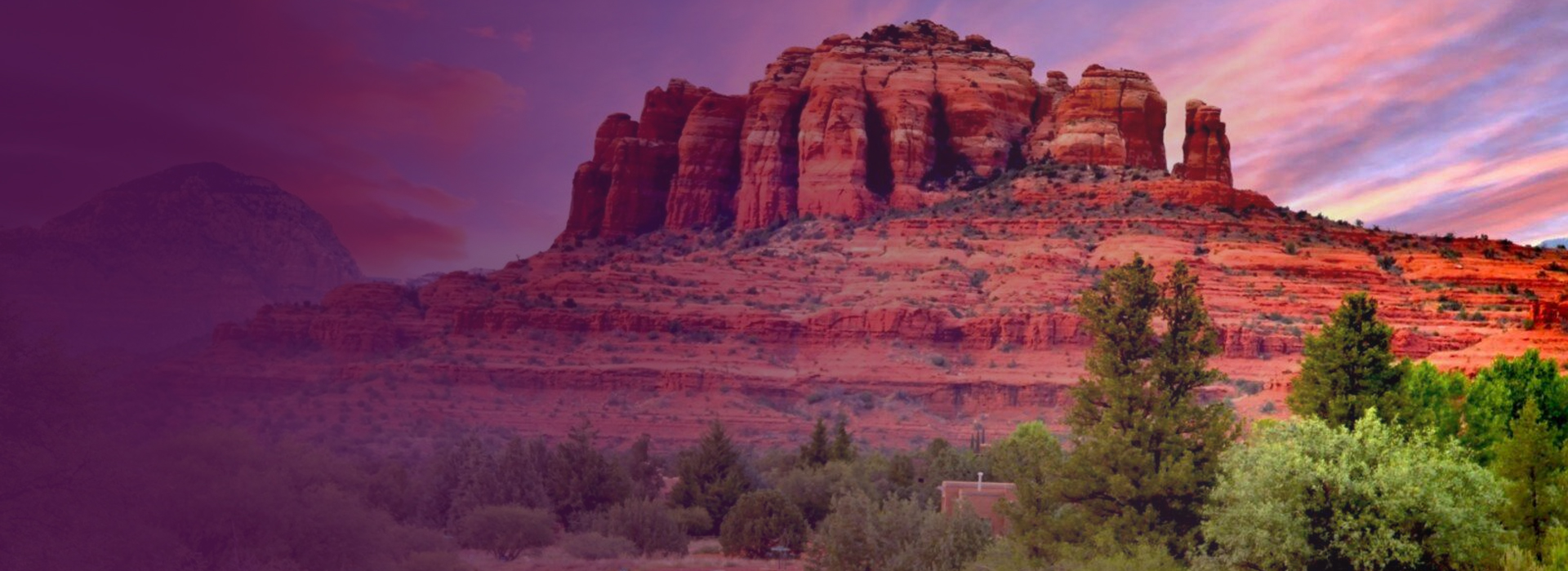 Red rock formation under a colorful sunset sky with green trees in the foreground.
