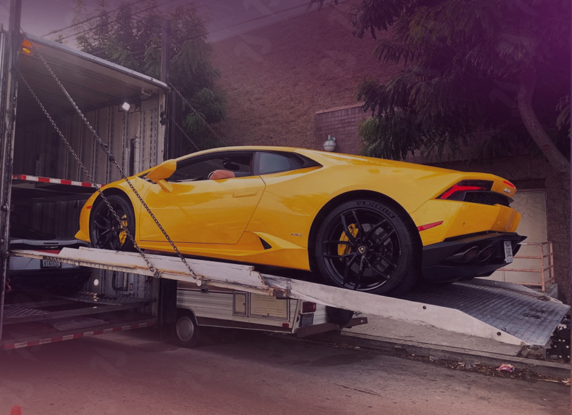 Yellow Lamborghini sports car being loaded onto a car carrier truck with chains securing the ramp.
