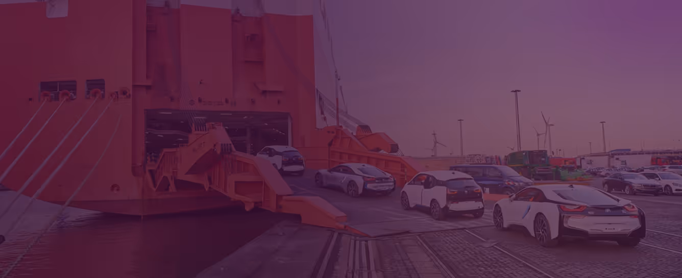 Electric cars disembarking from a large ship at a port with wind turbines in the background.