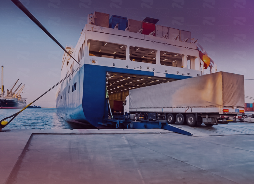 Semi-trailer truck boarding a large ferry ship at a dock during sunset.