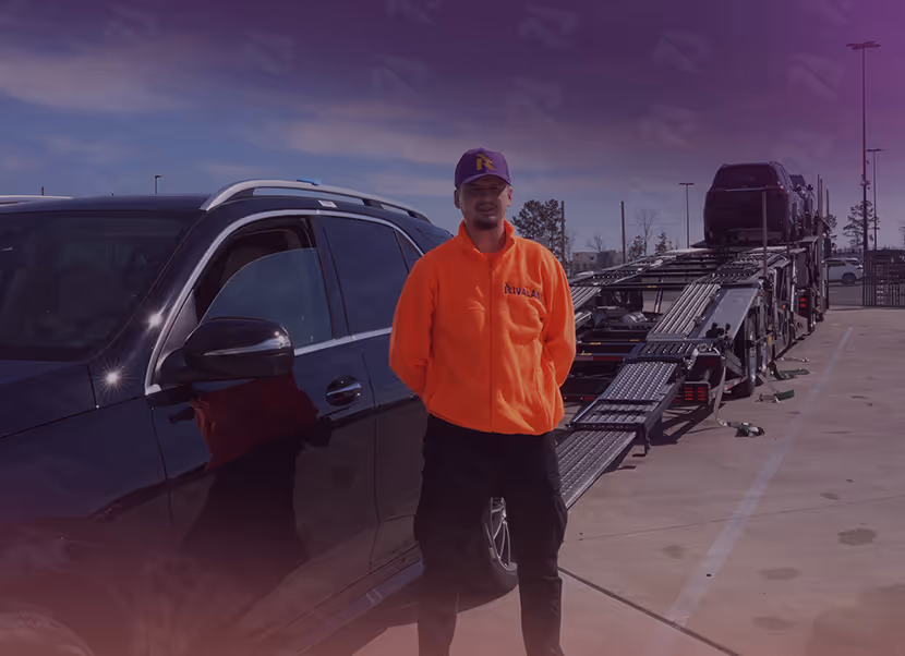 Man in an orange jacket and purple cap standing beside a black SUV and a vehicle transport trailer in a parking lot.