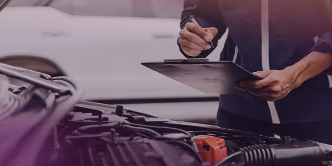 Person holding a clipboard and pen inspecting a car engine with the hood open.