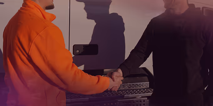 Two men shaking hands next to a white vehicle, one wearing an orange jacket and the other in a black jacket.