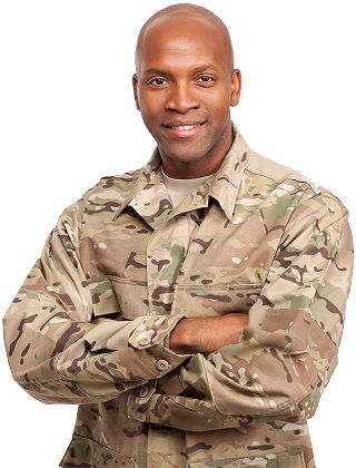 Service member in camouflage uniform standing with arms crossed in front of an American flag.