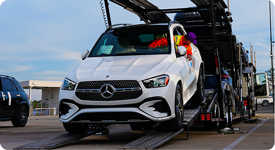 White SUV being loaded onto an open car carrier while a driver guides it up the ramp.