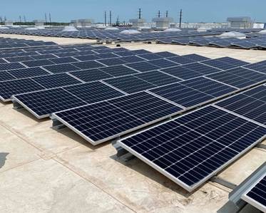 The image shows a large, organized solar panel array on a rooftop, with rows of solar panels installed and visible utility lines.AI-generated content may be incorrect.