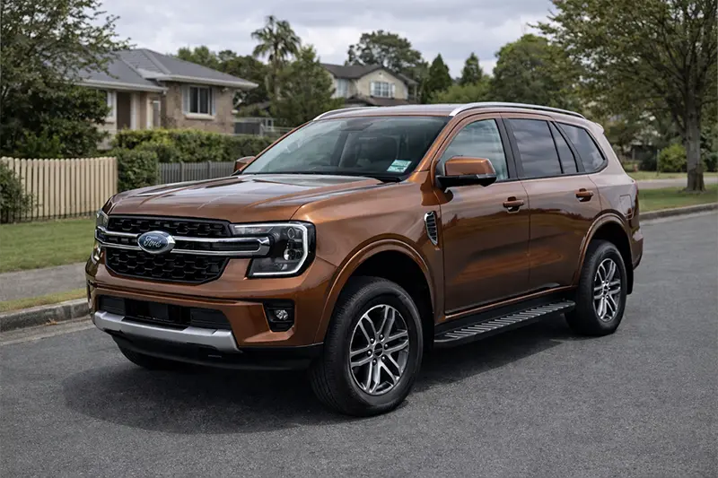 White Toyota RAV4 parked on a street near greenery with modern headlight design and chrome alloy wheels.