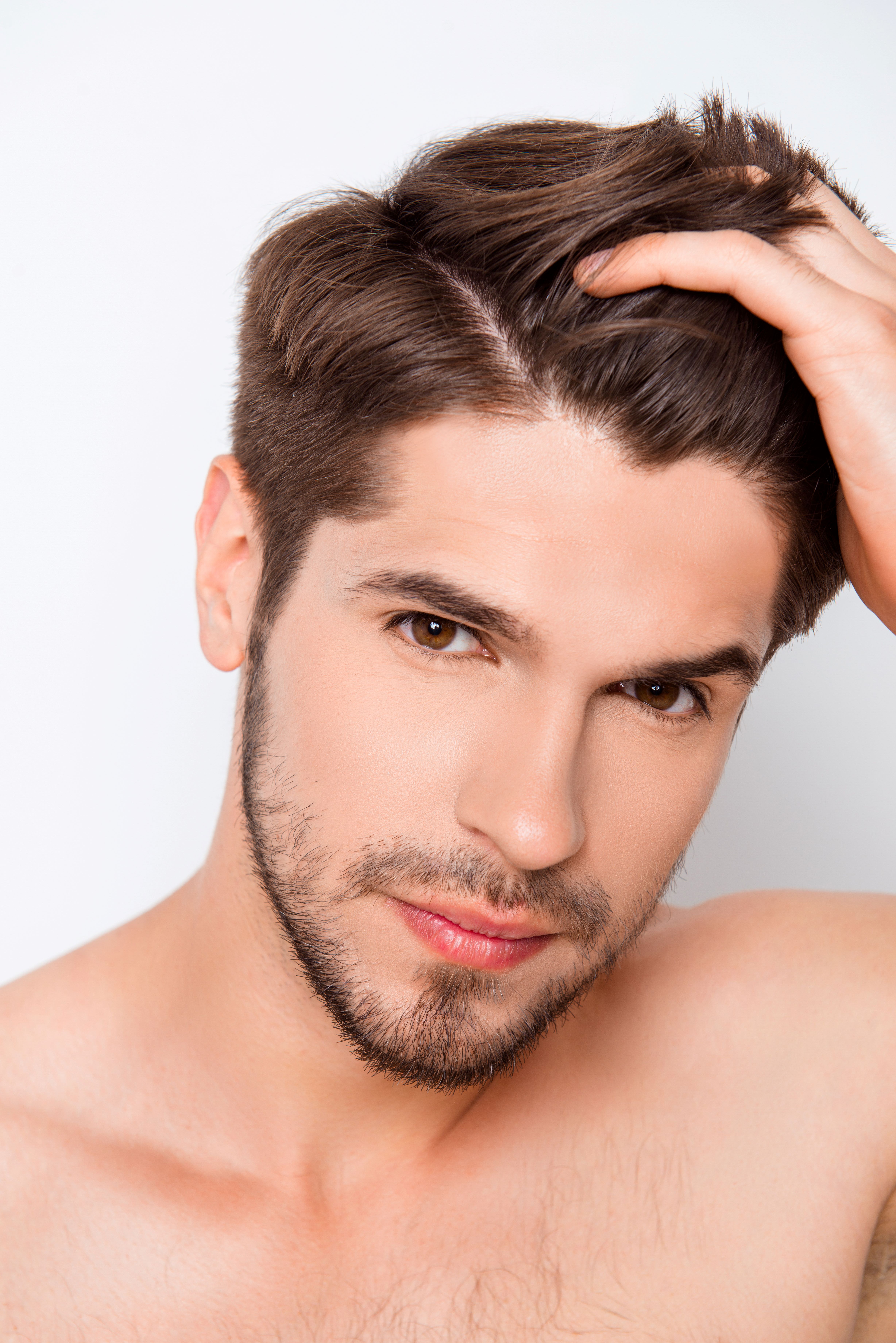A shirtless man is holding his hair in the air.