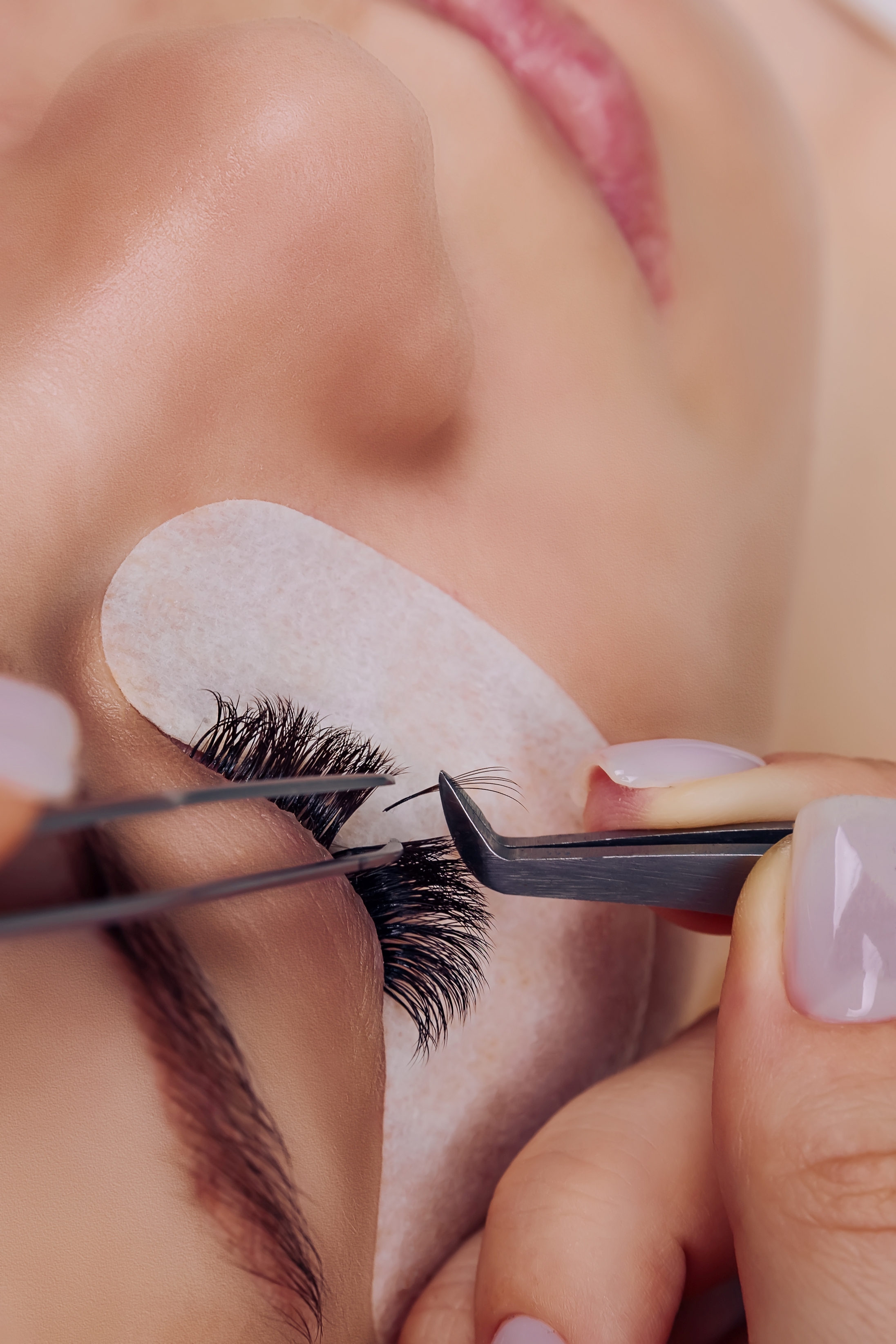 A woman getting her eyelashes done with a pair of scissors.