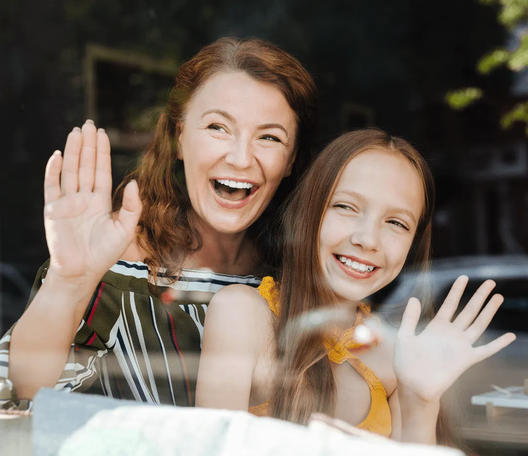 A woman and a young girl waving out a window.