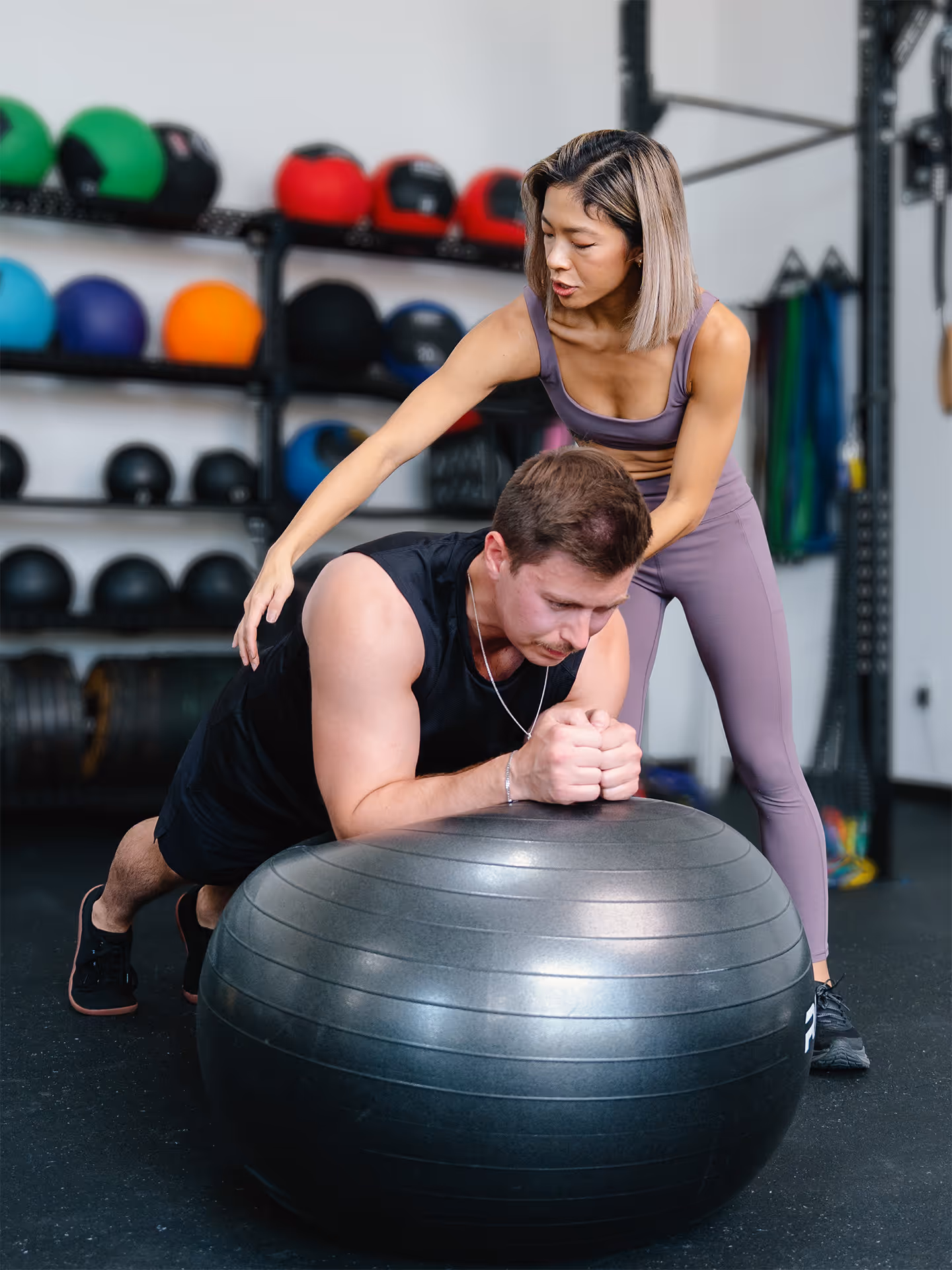 Aretha coaching a male athlete through a plank on a stability ball.