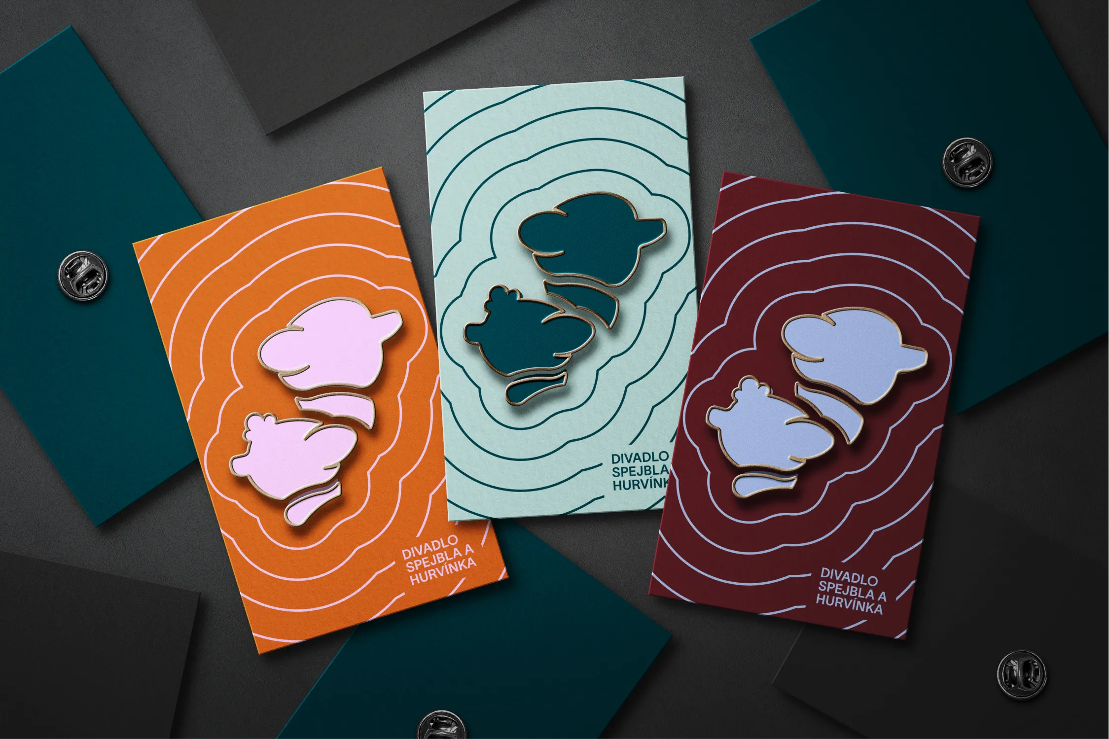 Three colorful enamel pins of cartoon character silhouettes displayed on matching abstract topographic-patterned cards labeled 'Divadlo Spejbla a Hurvínka'.