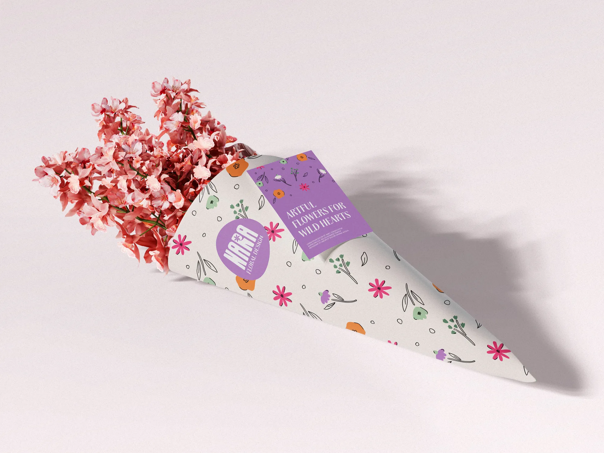 Bouquet of pink flowers wrapped in white paper with colorful floral patterns and a purple label reading 'Artful Flowers for Wild Hearts'.