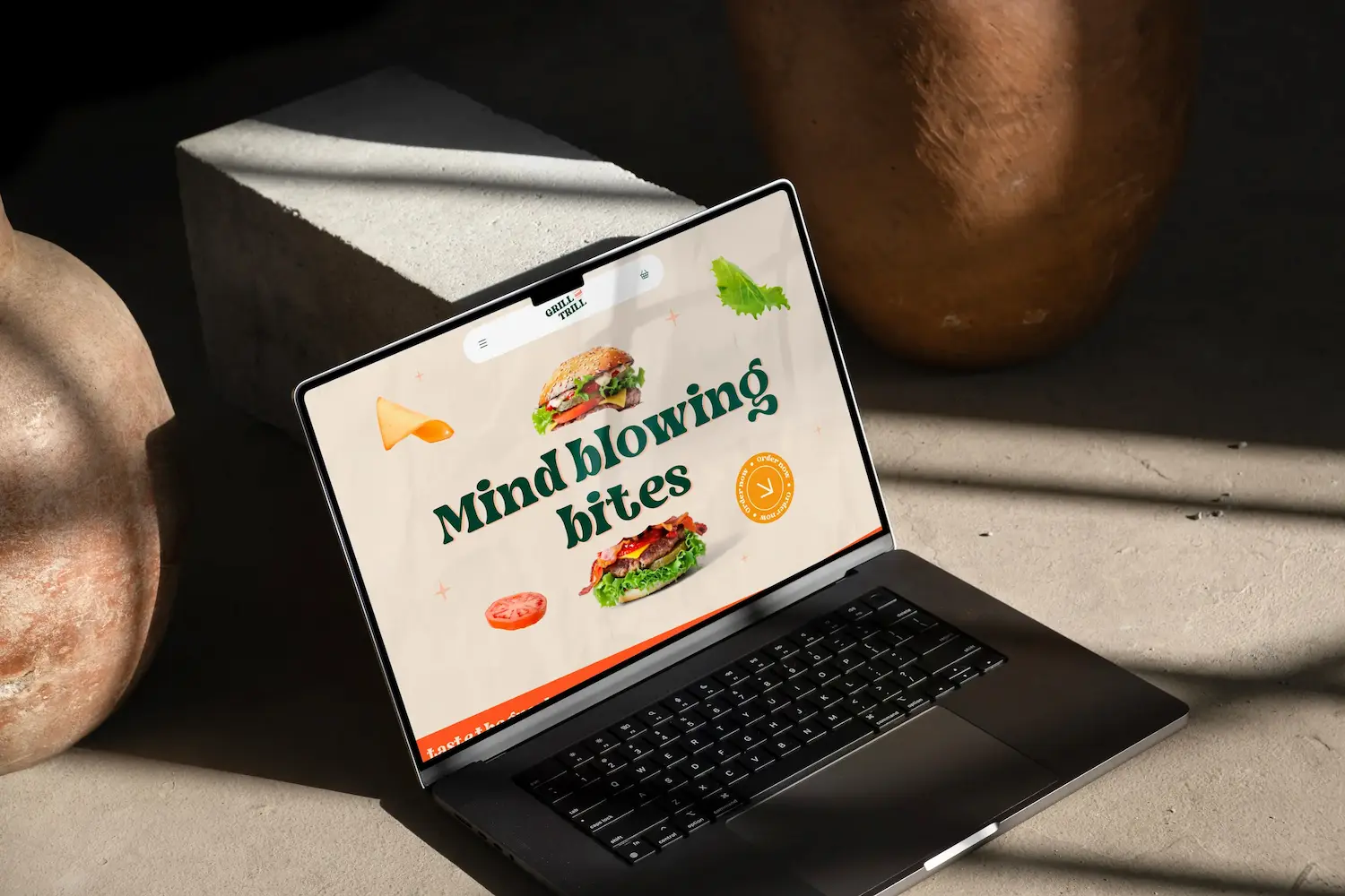 Open laptop on concrete surface displaying a food website homepage with 'Mind blowing bites' text and burger images.
