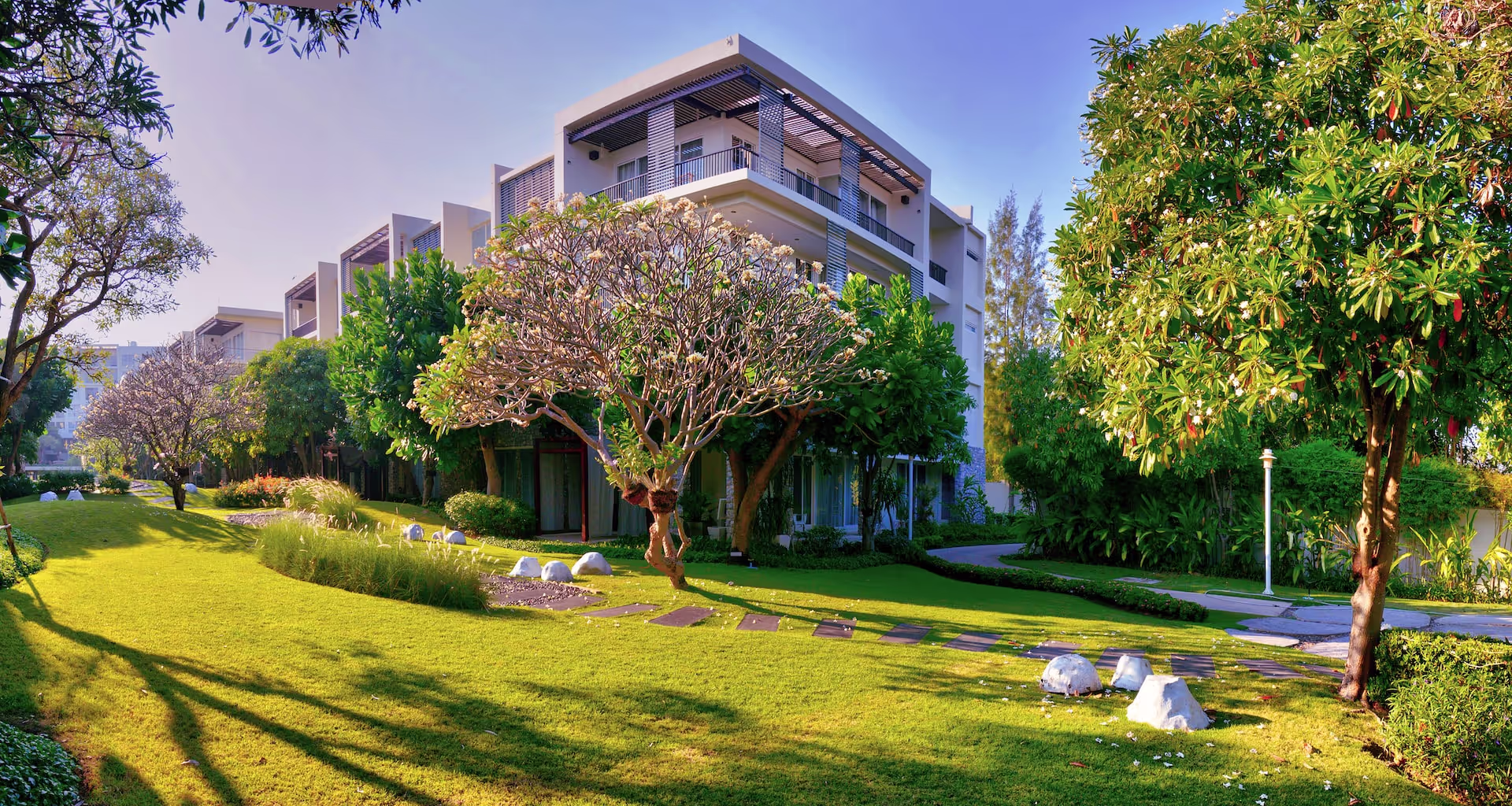 Luxuriöser Apartmentkomplex vor blauem Himmel, mit grünen Bäumen und einem riesigen Pool