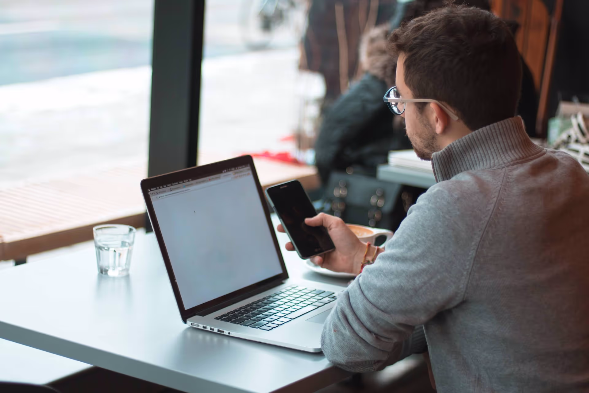 Ein Mann sitzt vor einem Laptop mit einem Smartphone in der Hand