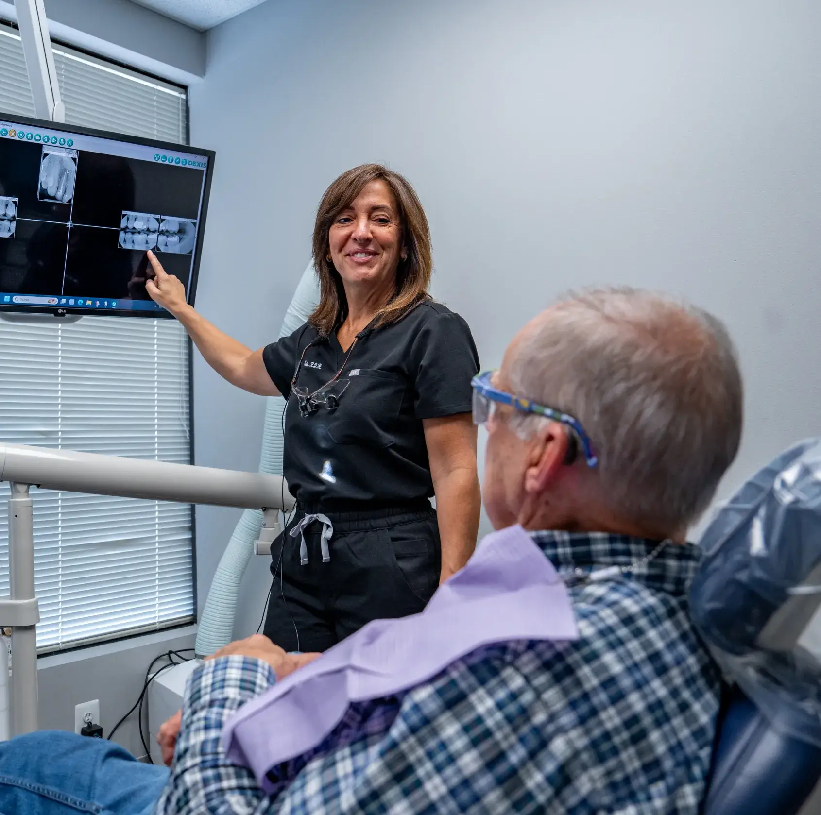 A woman in glasses and a blue sweater is thinking with her finger on her chin.