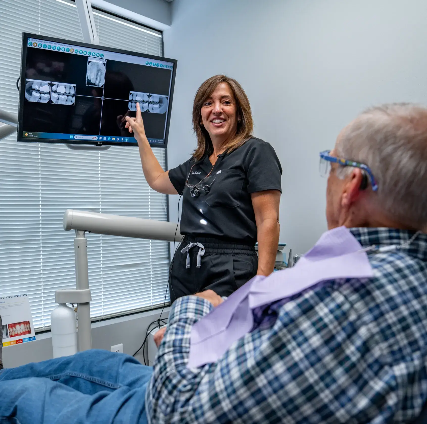 A dentist explains X-ray images to a patient sitting in a dental chair.