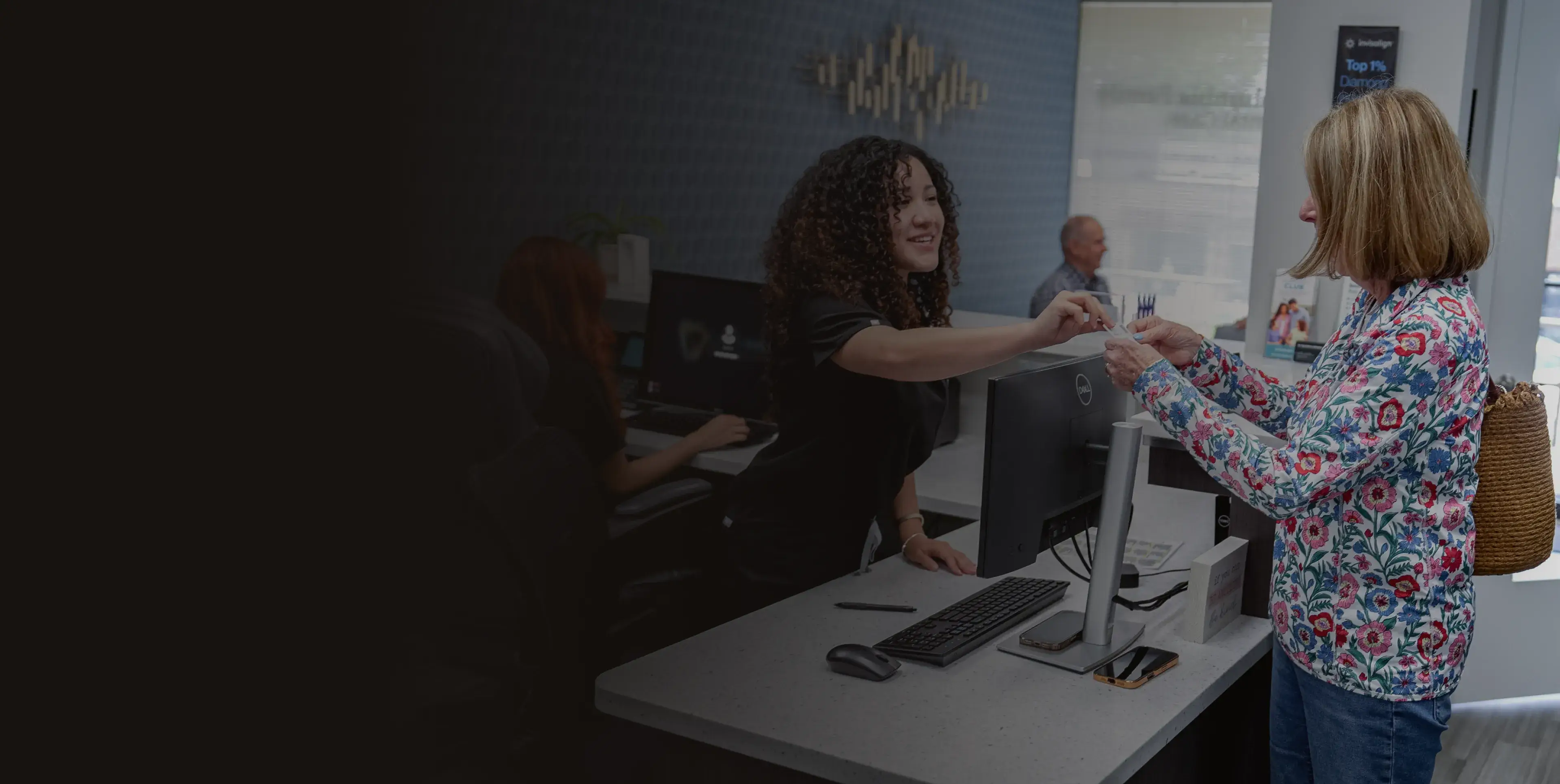 A woman at a desk hands a document to another woman standing beside her.