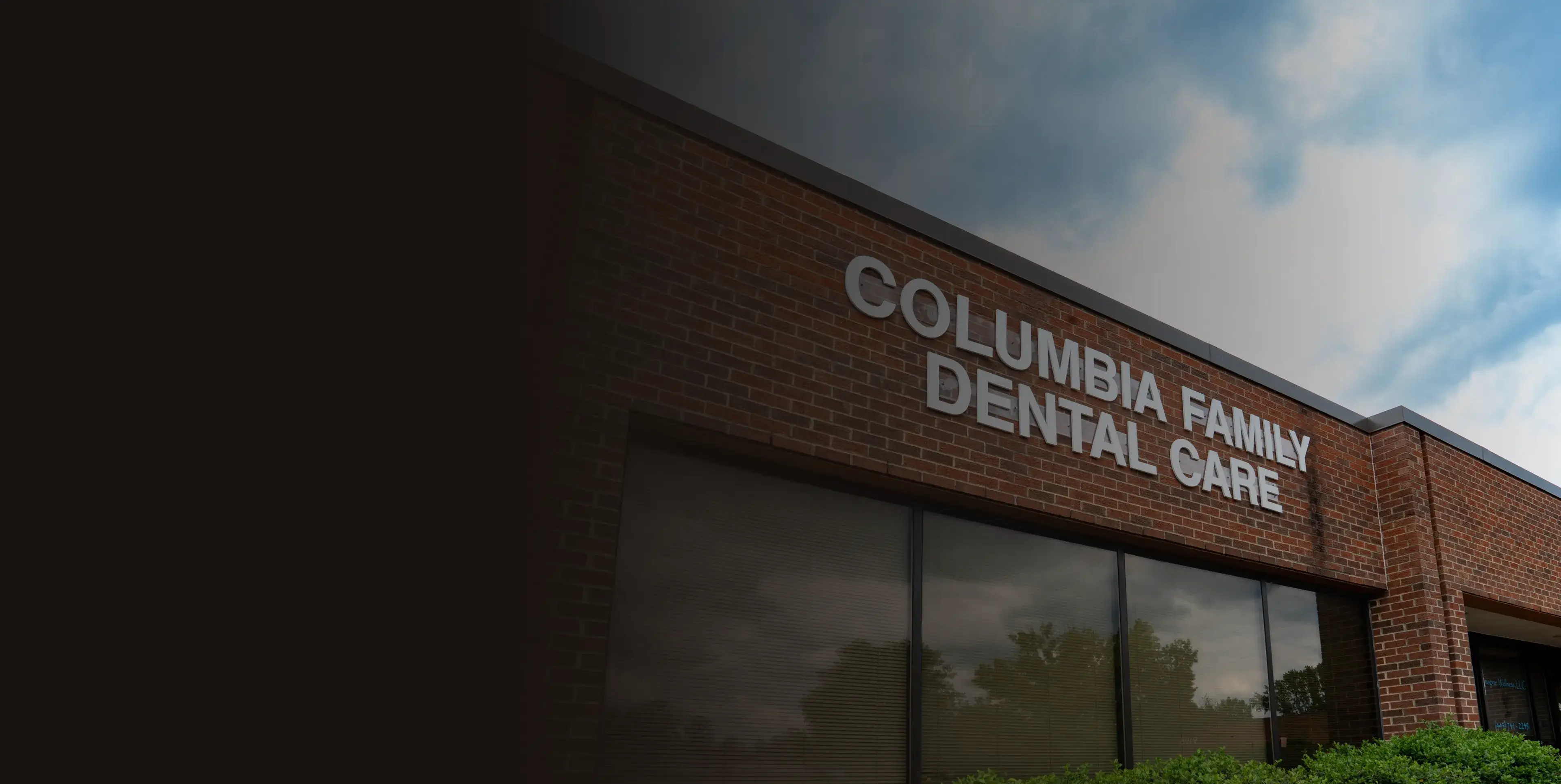 Brick building with sign reading "Columbia Family Dental Care" in white letters against a cloudy sky.