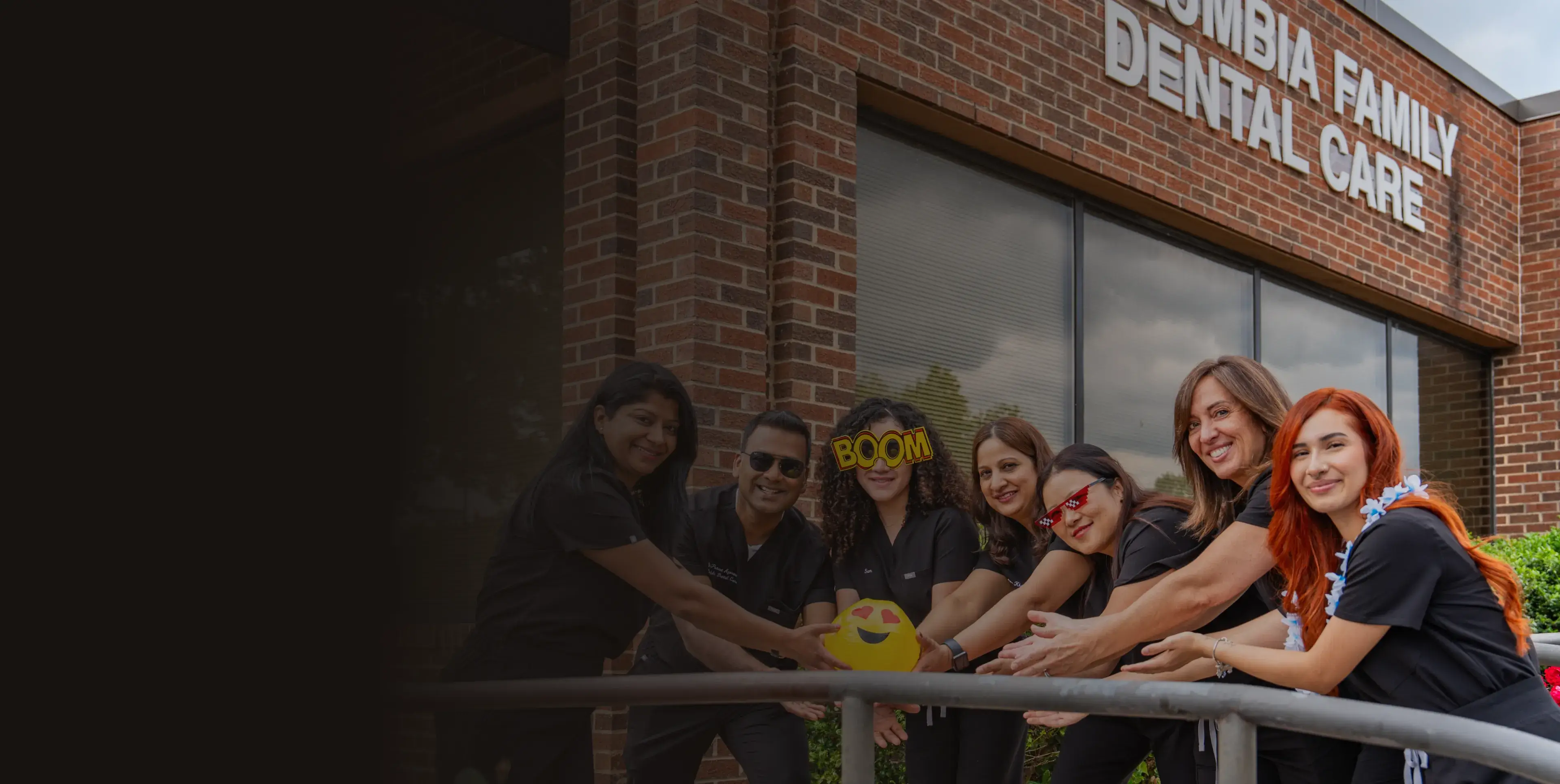 A group of people in uniforms smile and pose in front of a dental care office.