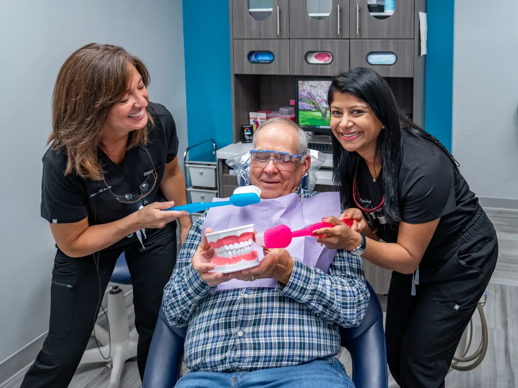 A man sitting in a dental chair gives two thumbs up, wearing a protective bib.