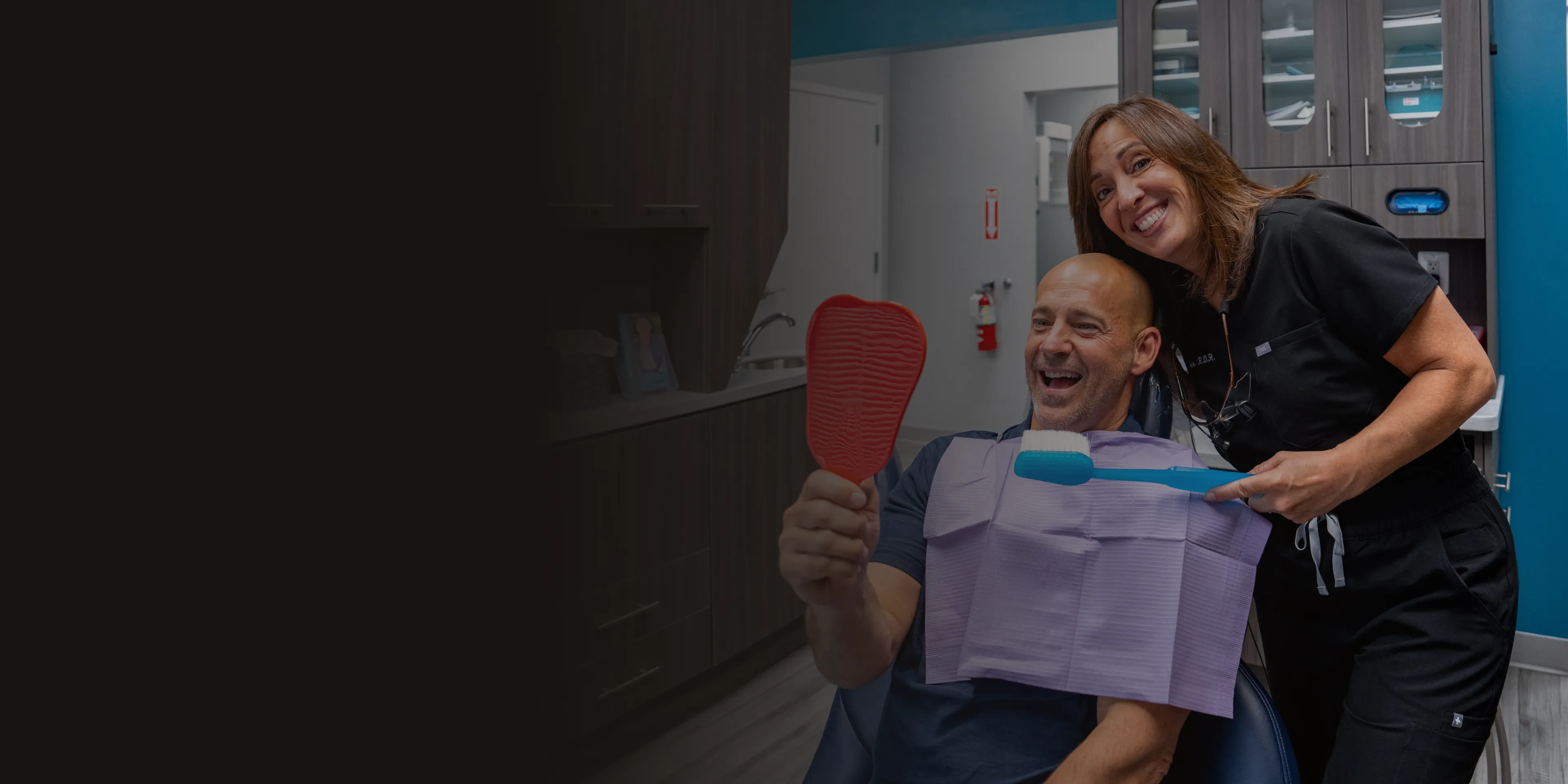 Man sitting in dental chair holding mirror, smiling, with dentist standing beside him.