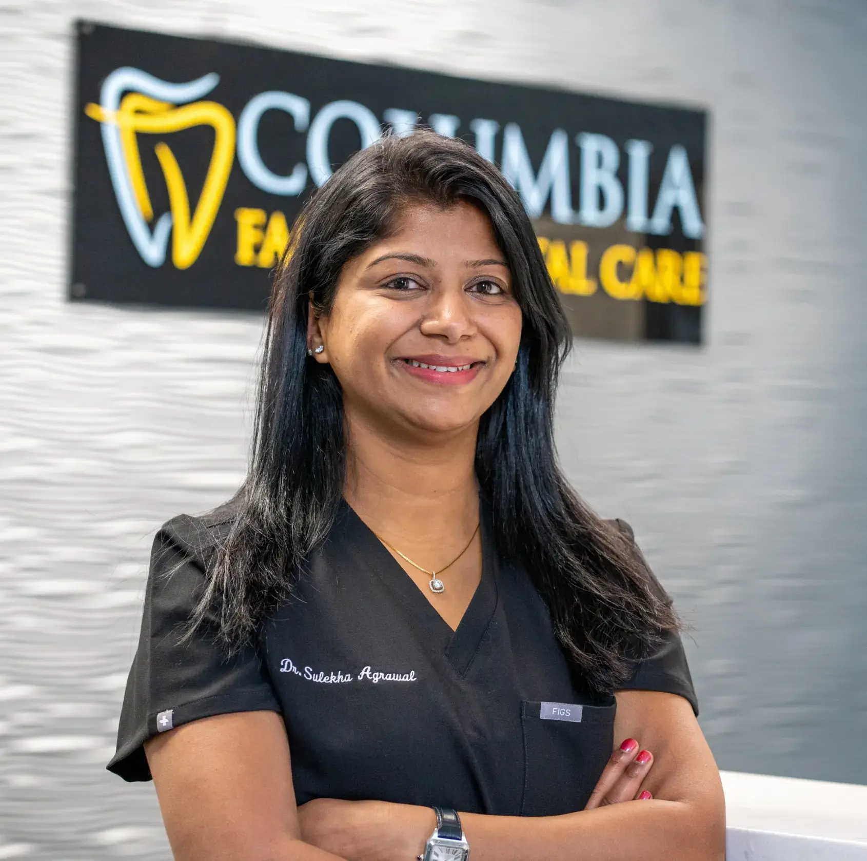 Dr. Sulekha Agrawal, in a black uniform stands smiling in front of a dental care sign.