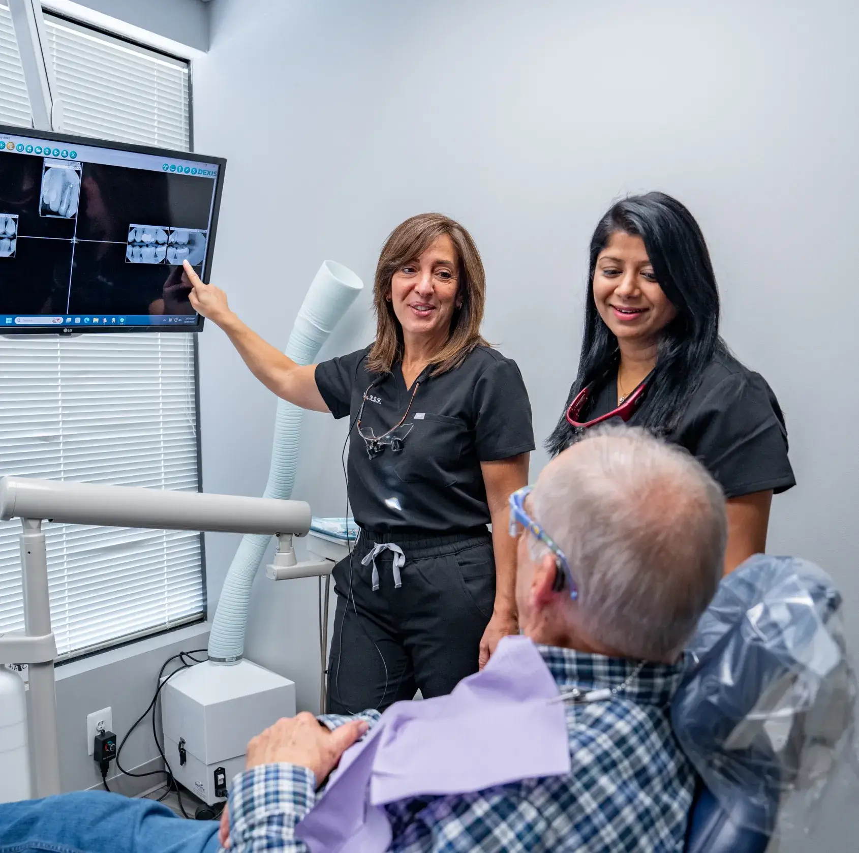 A patient wearing goggles receives a dental check-up from a dentist and assistant.