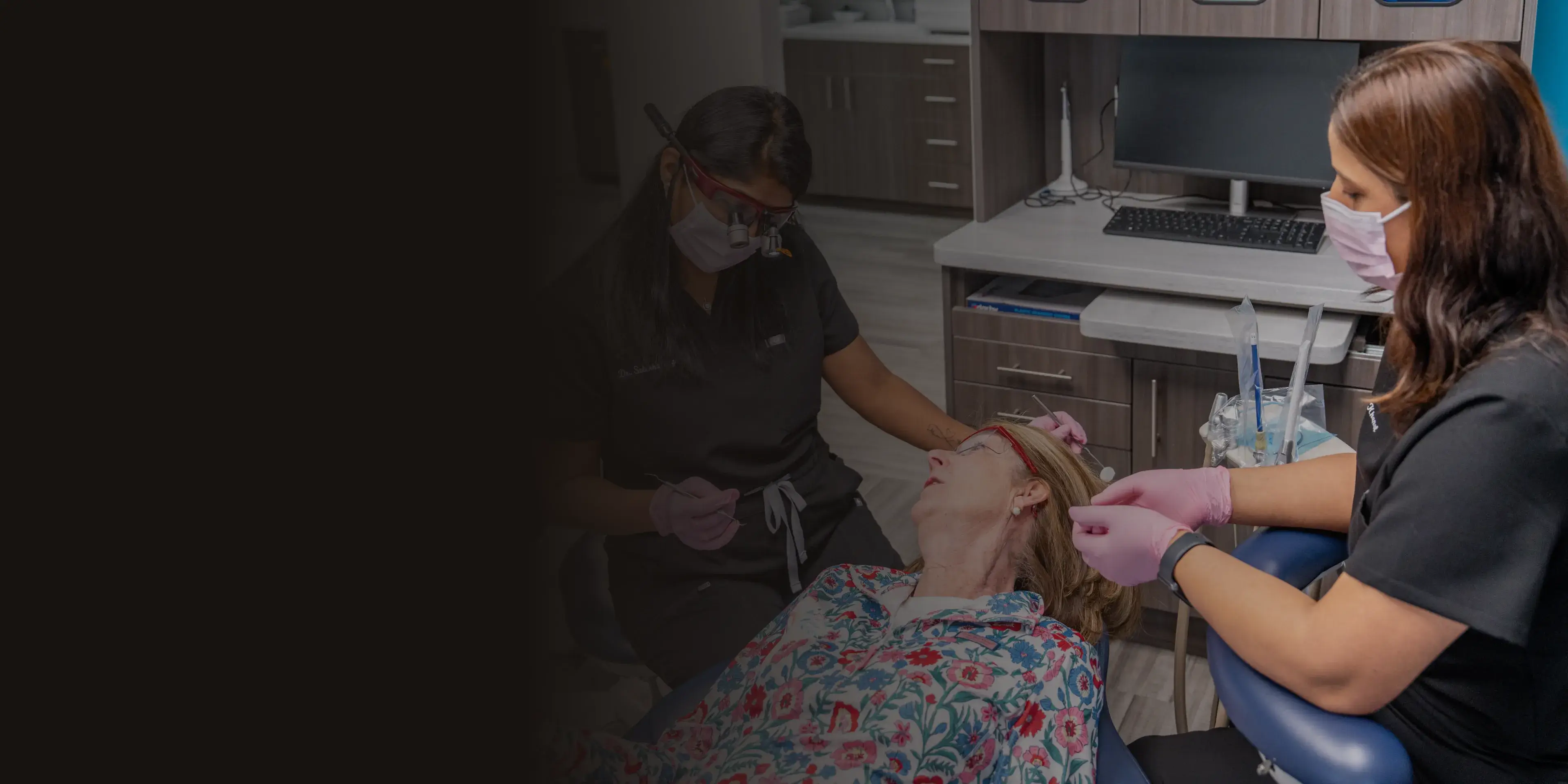 A woman playfully holds a large pink toothbrush near a smiling man's face in a dental office.