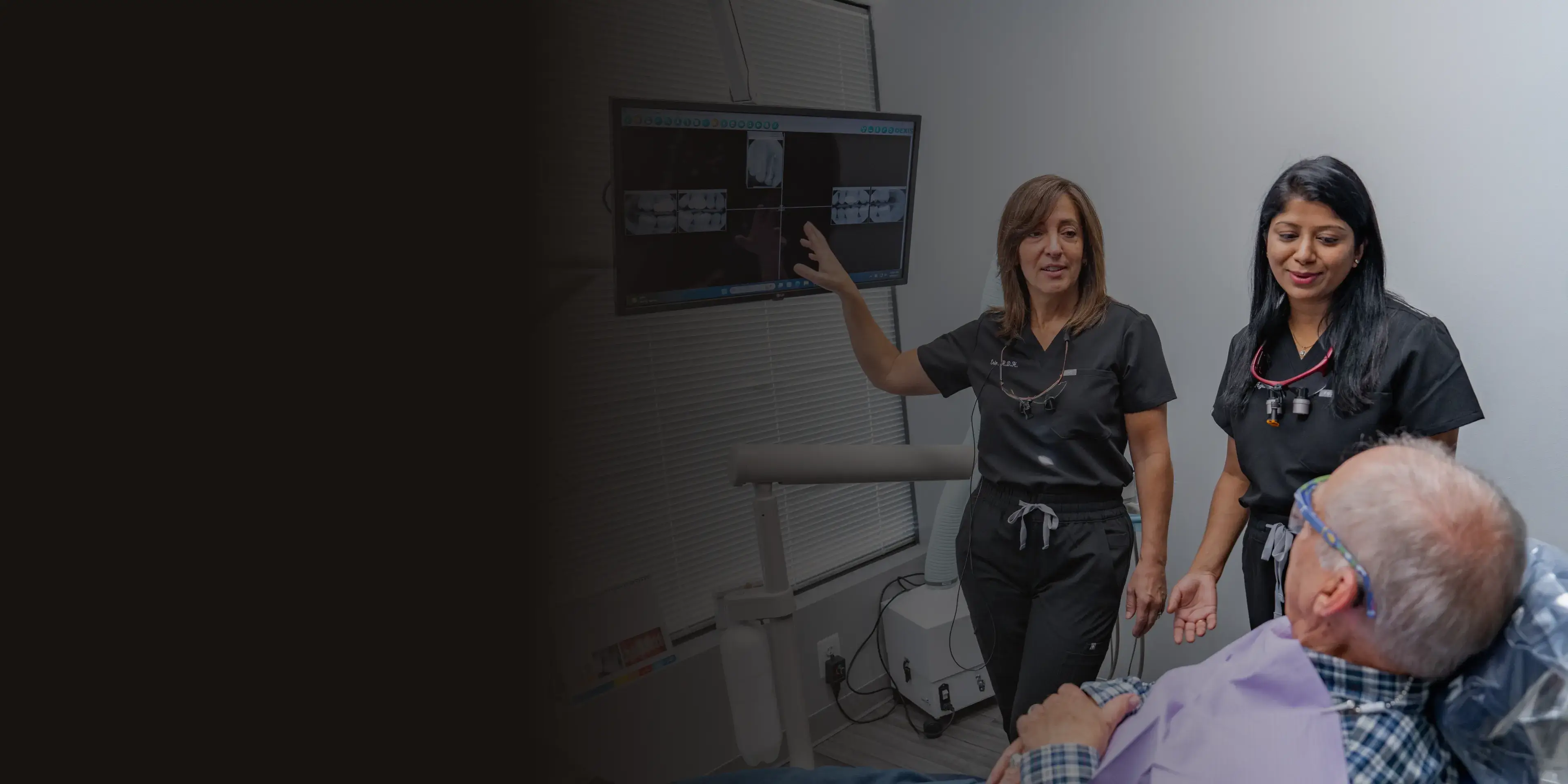Two dental professionals discuss X-rays with a patient sitting in a dental chair.