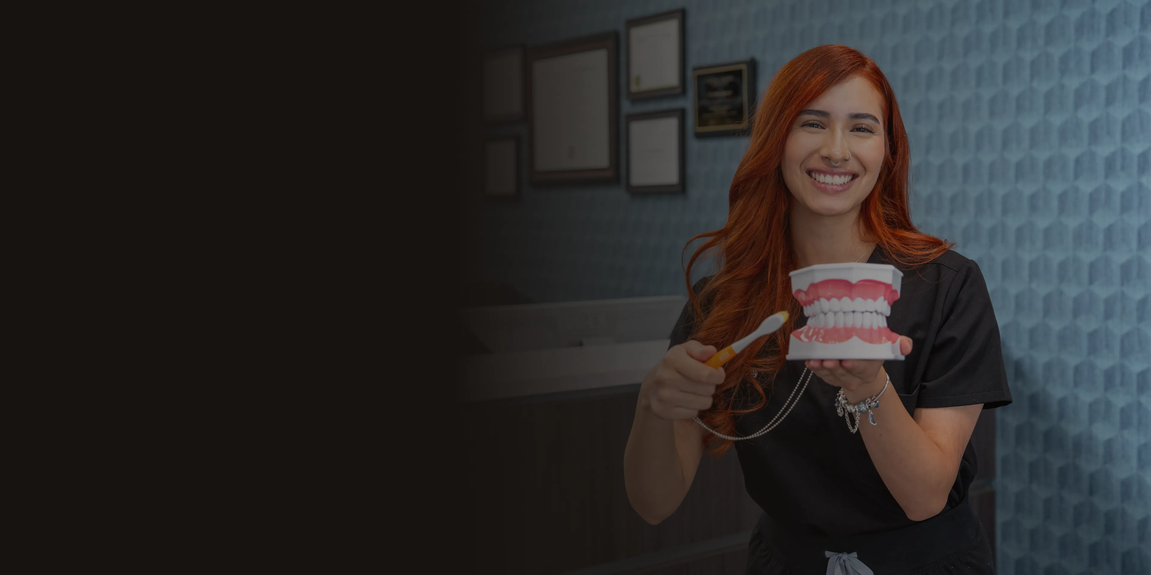 A smiling woman with red hair holds a dental model and toothbrush, demonstrating brushing.