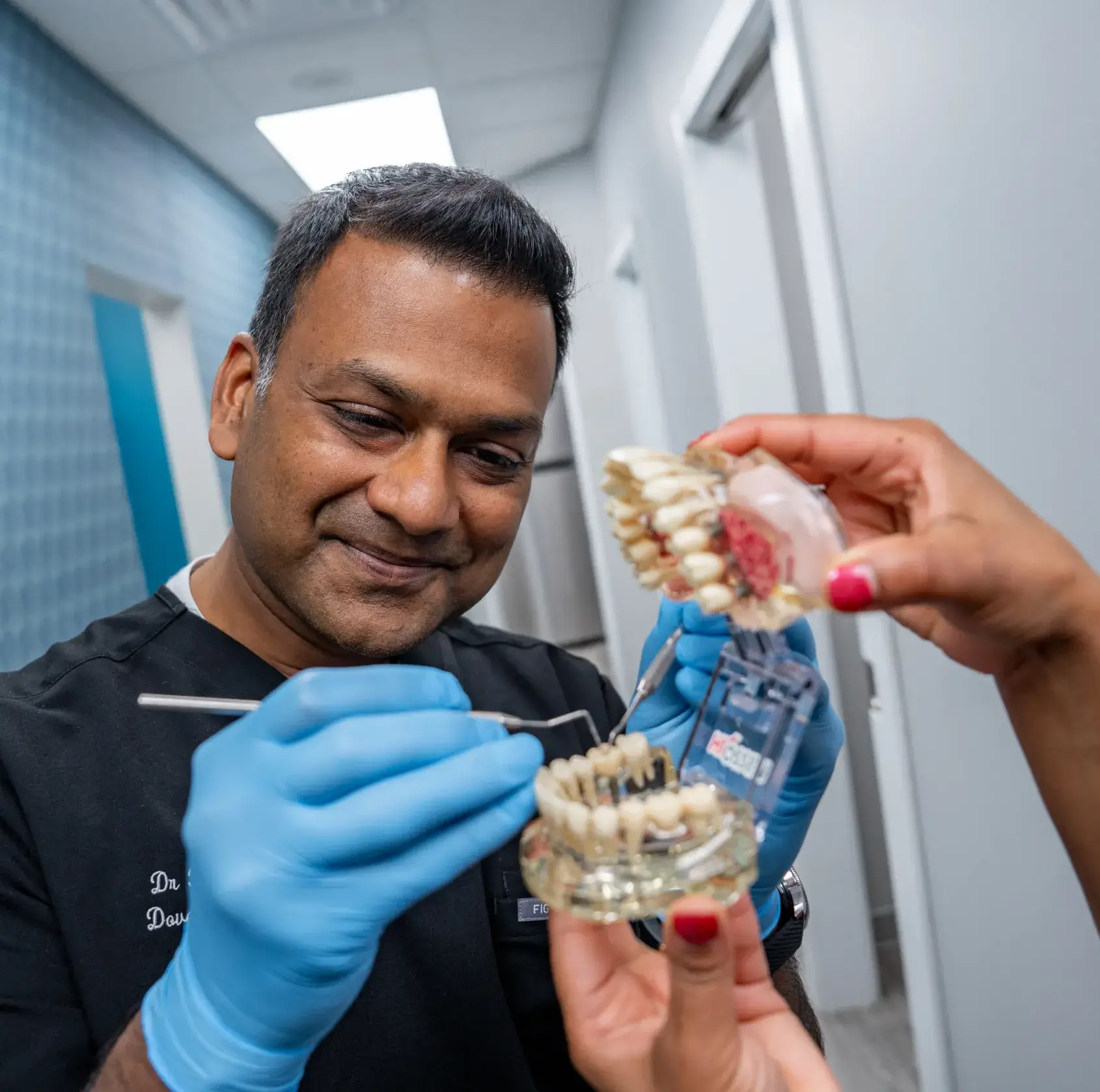 An older man holds a large dental model showing a full set of teeth.