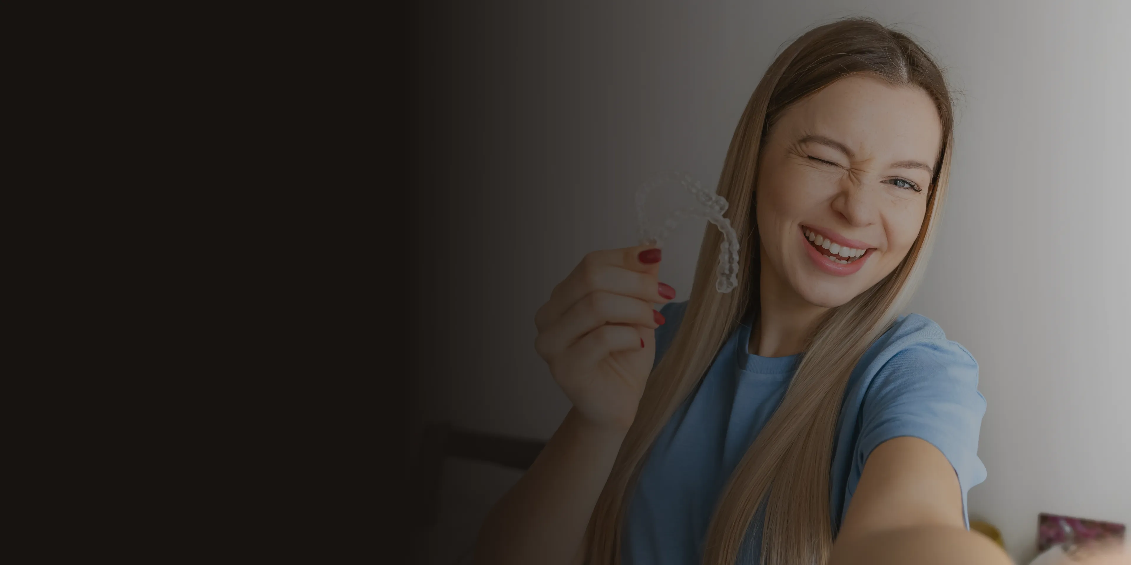 A woman smiles while holding a dental retainer in her hand.