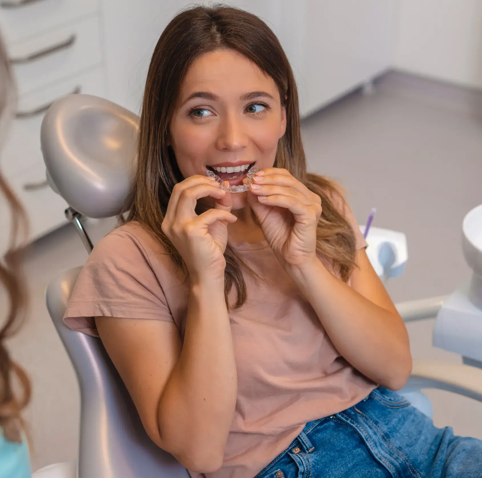 A woman in a dental chair tries on a clear orthodontic aligner.