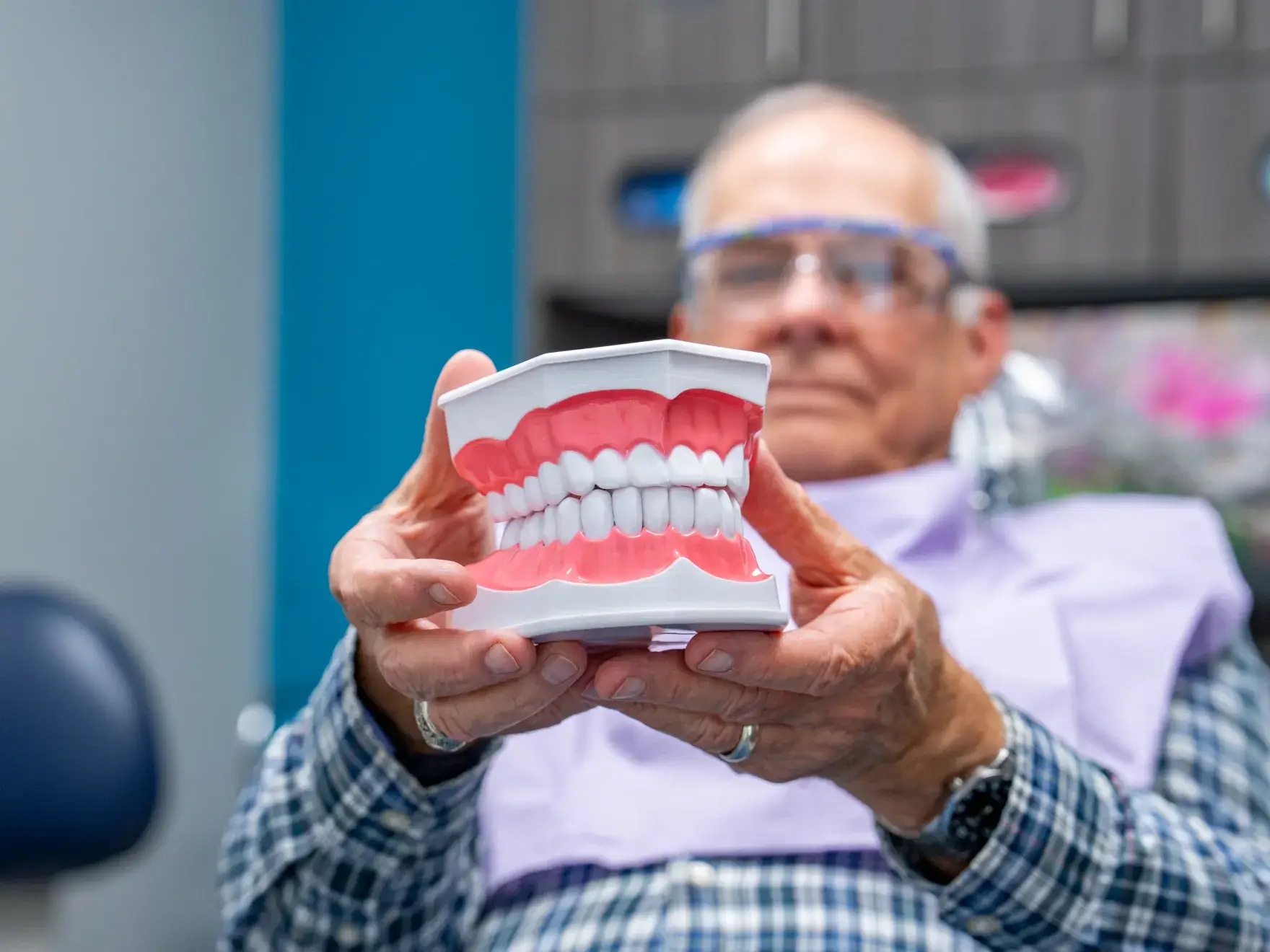 A person holds a model of large teeth in a dental office.