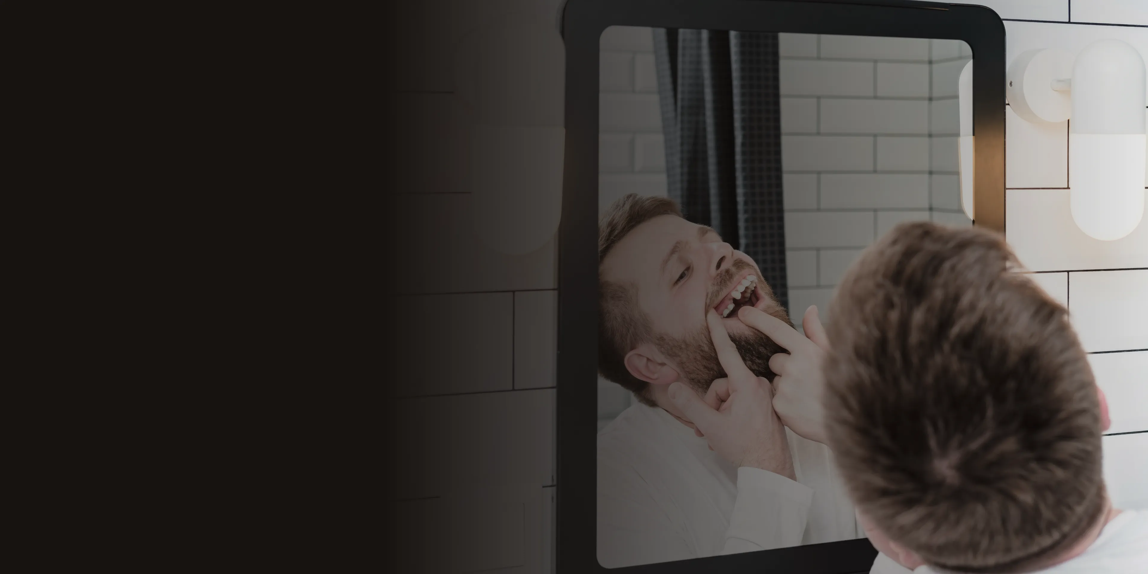 A man stands in front of a mirror, flossing his teeth with both hands.