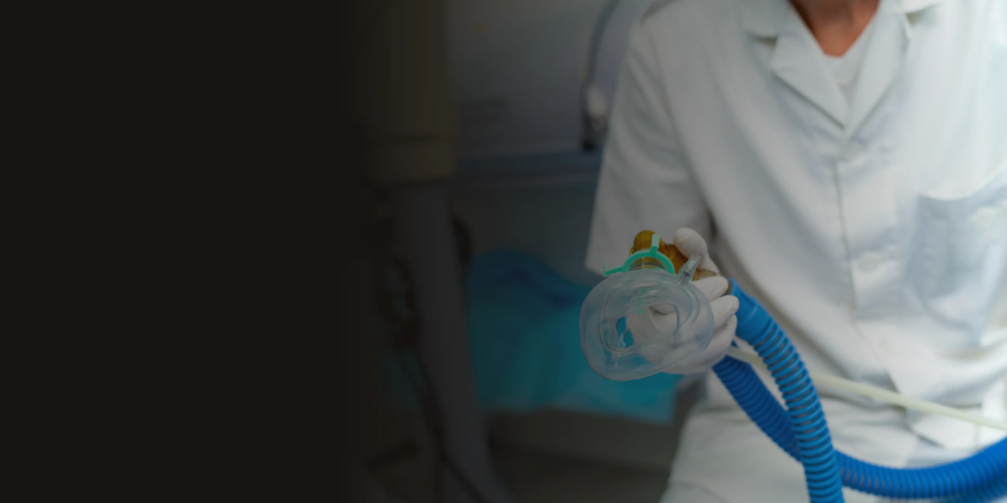 Person in a lab coat holding a medical breathing mask with a blue hose.